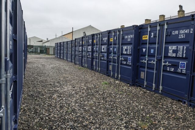 A clean gravel driveway between two rows of navy blue MB Storage containers
